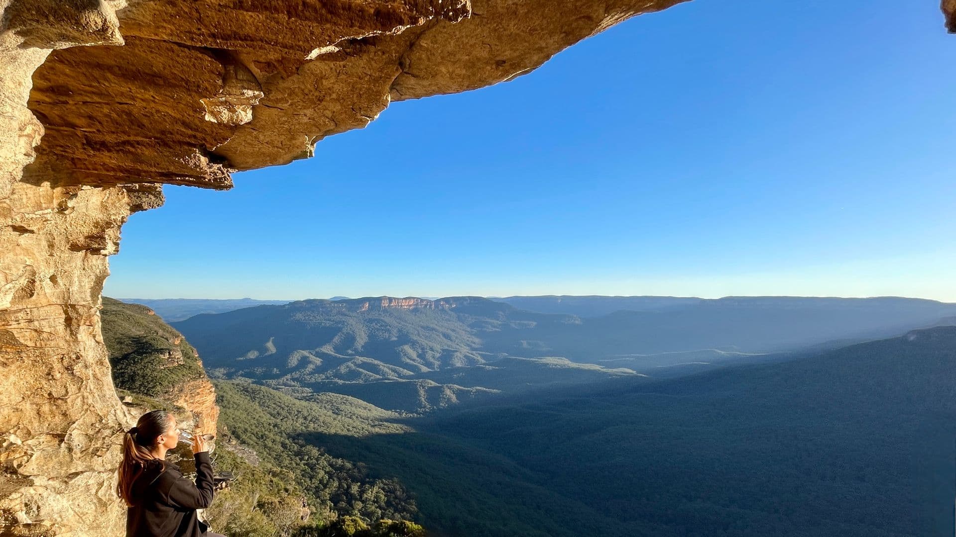 Woman sipping champagne in a cave lookout above the Jamison Valley, Blue Mountains, on a private tour.