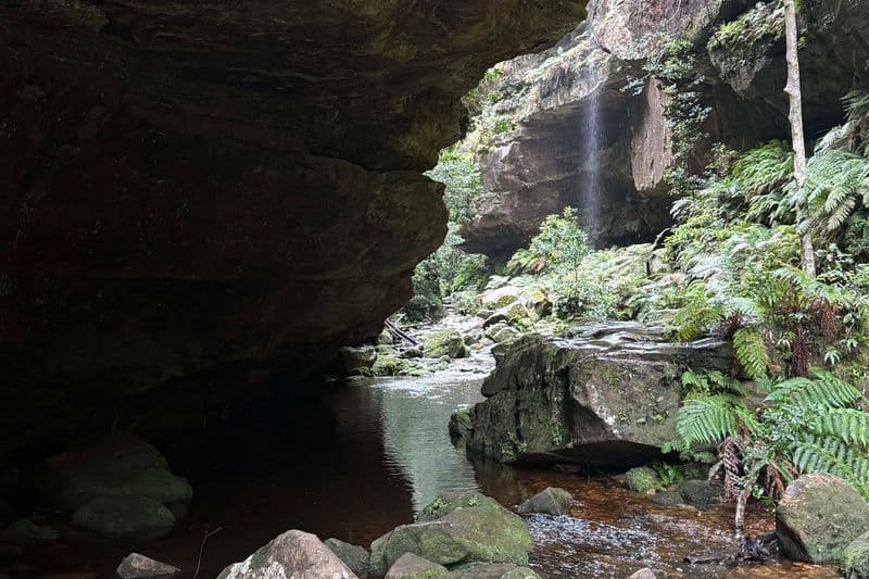 Crystal-clear creek pool beneath overhanging sandstone cliffs with a cascading waterfall, Grand Canyon Walk, Blue Mountains NSW