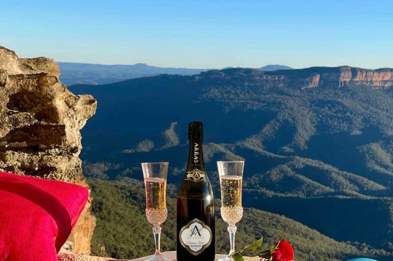 Champagne picnic spread at a secret Blue Mountains cave with sweeping Jamison Valley views on a clear sunny day.