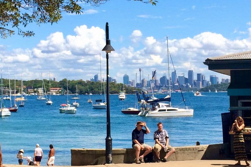 Sydney Harbour viewed from Watsons Bay, city skyline and harbour bridge visible across calm blue water