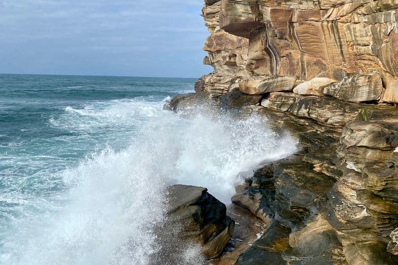 Large wave crashing into sandstone cliffs near Bronte Beach, Sydney — dramatic coastal scenery on the Eastern Suburbs coastline.