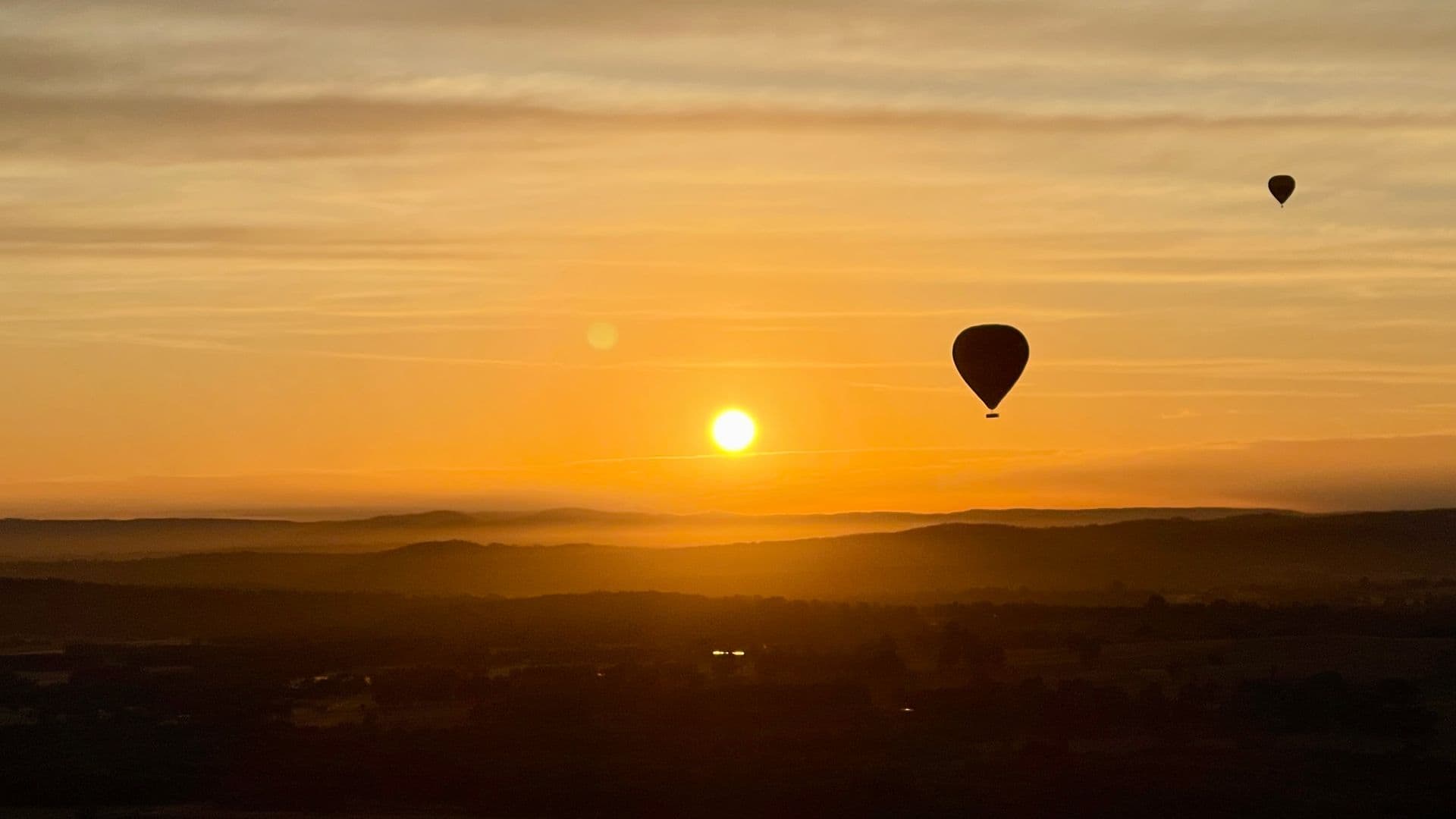Hot air balloon floating over Hunter Valley vineyards at sunrise, golden light across rolling wine country landscape