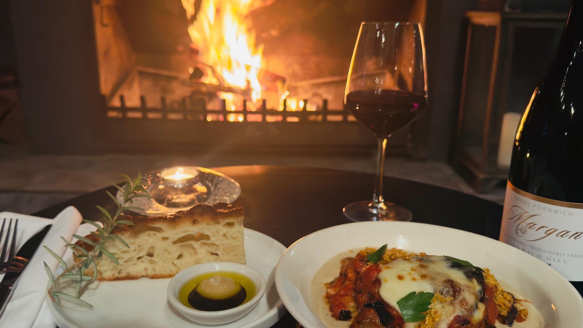 Food and wine spread beside a roaring wood fire fireplace at Estate Tuscany, Hunter Valley, NSW.