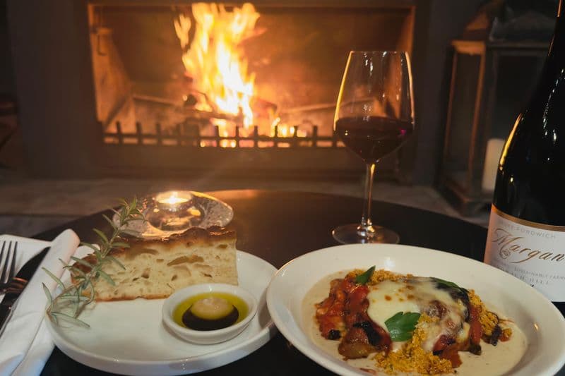 Food and wine spread beside a roaring wood fire fireplace at Estate Tuscany, Hunter Valley, NSW.